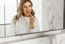 Woman applying lip gloss in mirror.